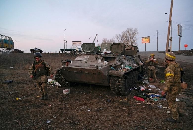 Các binh sĩ Ukraine bên cạnh chiếc xe bọc thép được cho là của quân đội Nga, bị phá hủy, bên ngoài Kharkiv, Ukraine, ngày 24/2. (Nguồn: Reuters)