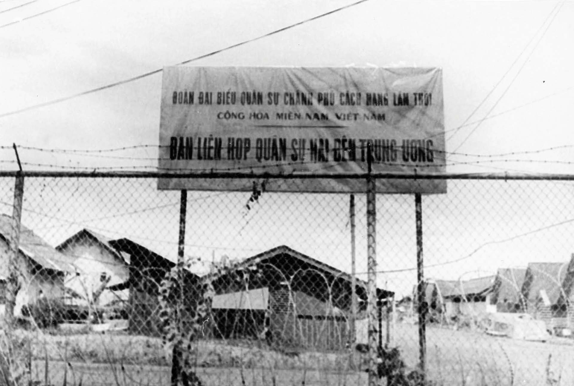 Tấm biển đề dòng chữ “Đoàn Đại biểu Chính phủ Cách mạng Lâm thời Cộng hòa miền Nam Việt Nam, Ban Liên hợp quân sự  hai bên Trung ương” đặt bên trong hàng rào kẽm gai gần cổng Trại Davis.