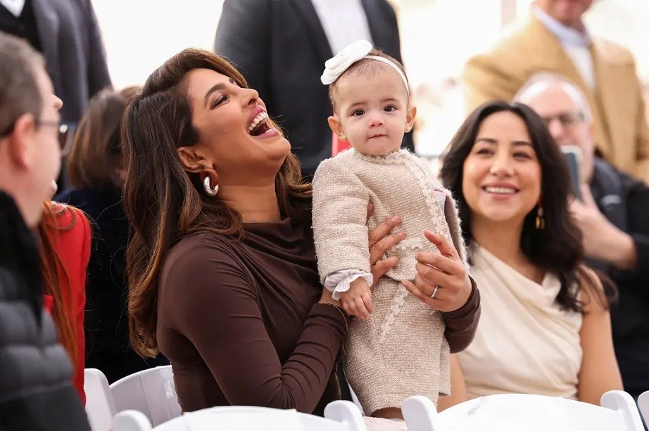 Hoa hậu Priyanka bế con gái Malti, ngồi hàng ghế đầu dự buổi lễ tại Hollywood hôm 30/1. Công chúa nhỏ diện bộ tweet màu kem xinh xắn, đội nơ trắng làm điệu. Cô bé trông đầy háo hức và hiếu kỳ khi đứng giữa chốn đông người.