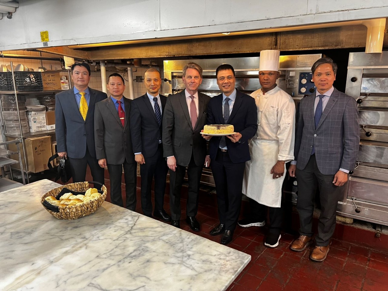 Đại sứ Đặng Hoàng Giang nhận quà lưu niệm từ Tổng Giám đốc khách sạn và anh Trần Văn Chanh – thợ bánh mang nửa dòng máu Việt đã làm việc tại lò bánh này 22 năm qua.