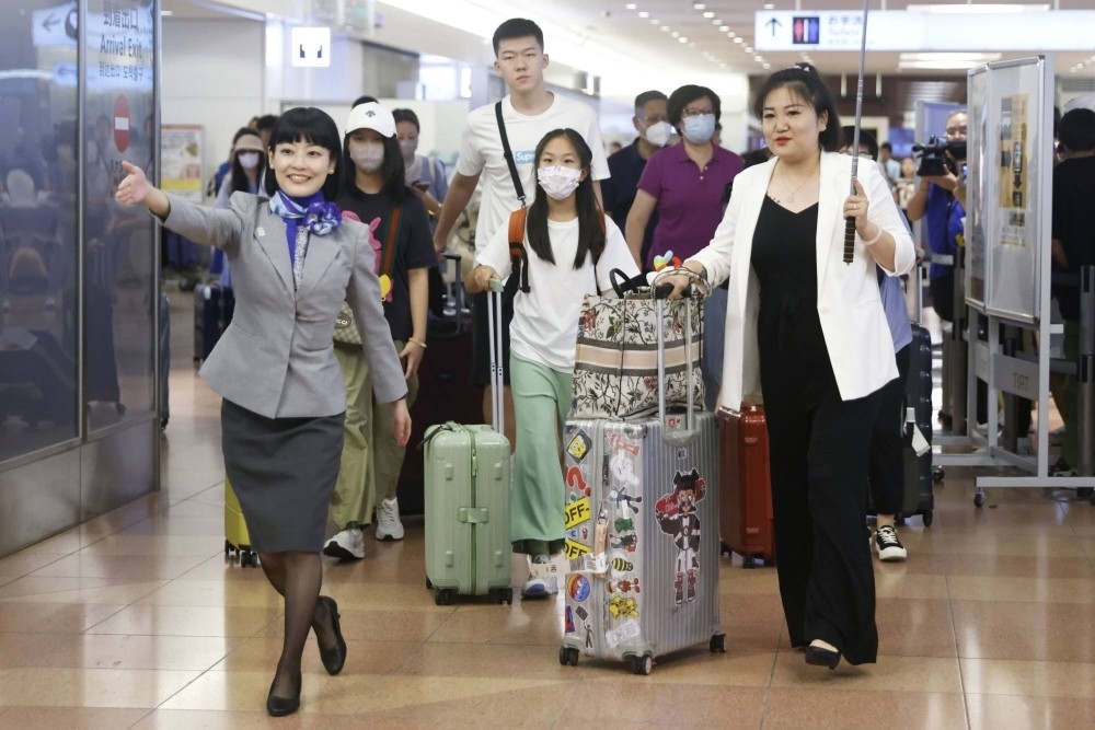 Một nhân viên của All Nippon Airways (trái) hướng dẫn một nhóm du khách Trung Quốc tại sảnh đến của Sân bay Haneda, Tokyo tháng 8/2023. (Nguồn: Bloomberg)