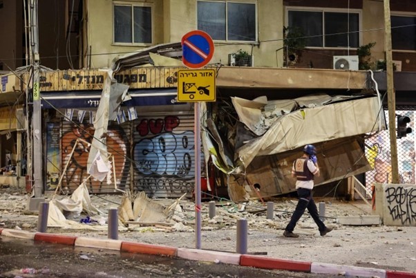 Một nhân viên cứu hộ Israel đi trước một cửa hàng bị hư hại ở Tel Aviv. (Nguồn: AFP)