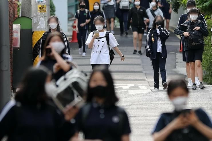 Students walk while looking at their mobile phones near a middle school in Seoul in this 2022 file photo. A bill has been proposed to restrict the use of mobile phones in schools. Newsis