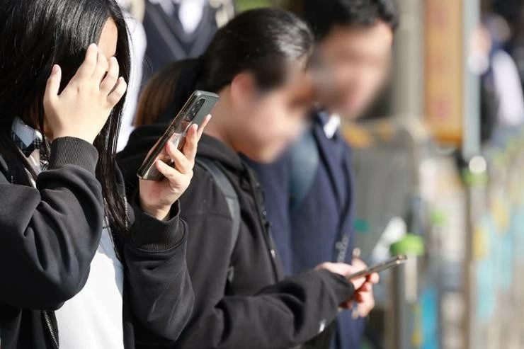 Students use smartphones while heading home outside a middle school in Seoul, Nov. 4. Yonhap