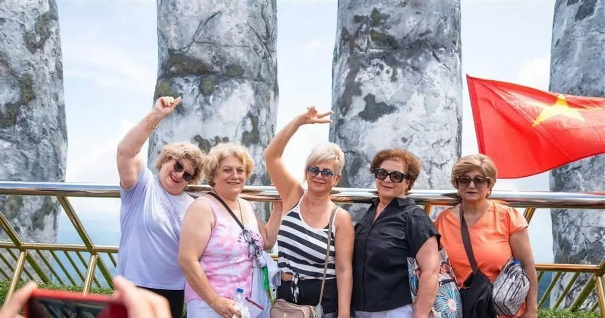 Du khách nước ngoài thích thú check-in với cây cầu Vàng được trang hoàng rực rỡ cờ Tổ quốc tại khu du lịch. (Nguồn: TTXVN)