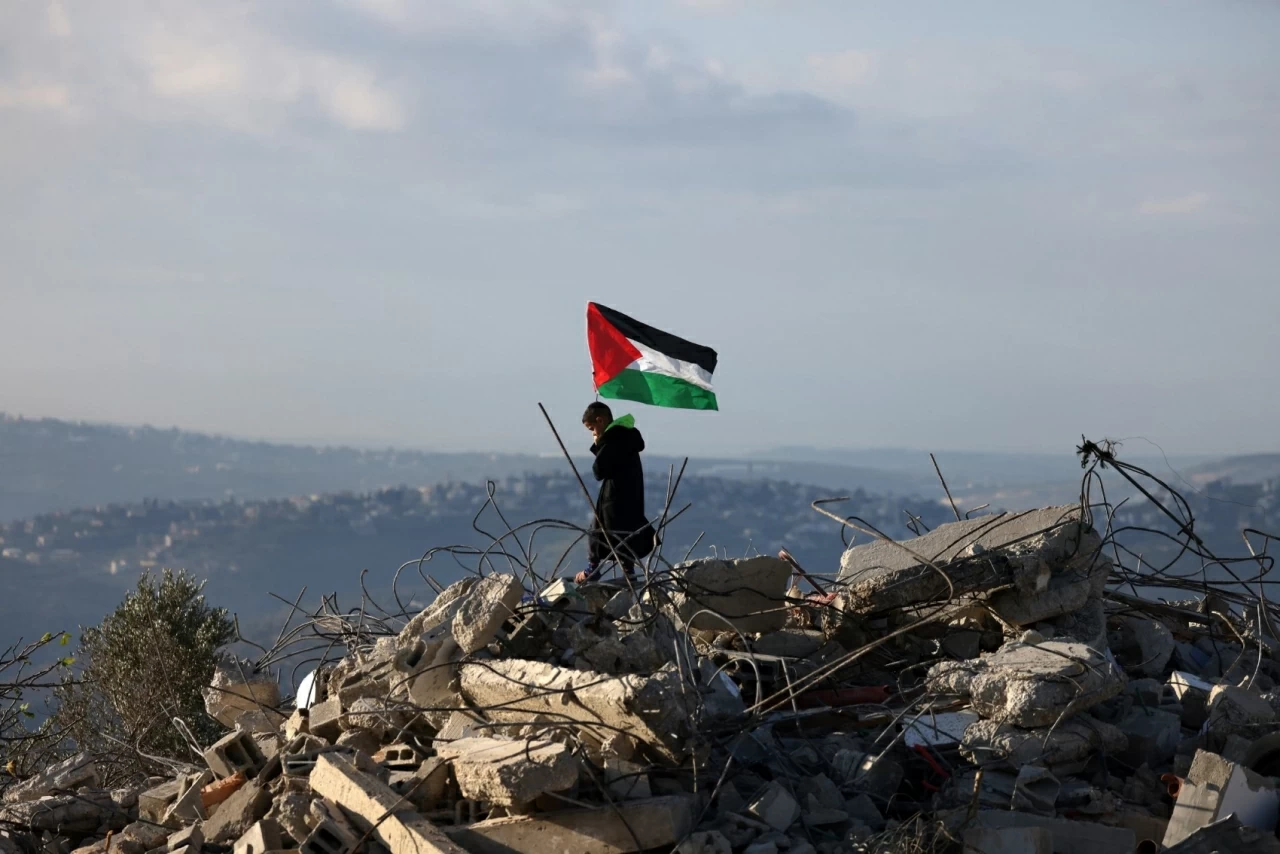 Một cậu bé vẫy lá cờ Palestine trên đống đổ nát của ngôi nhà thuộc gia đình Malik Ismail Salem tại làng Bizarya, gần thành phố Nablus ở Bờ Tây. Mười bốn quốc gia, trong đó có Anh, Canada và Đức, đã lên án việc nội các an ninh Israel phê duyệt 19 khu định cư mới tại Bờ Tây bị chiếm đóng, cho rằng động thái này vi phạm luật pháp quốc tế và có nguy cơ làm gia tăng bất ổn. (Nguồn: EPA)