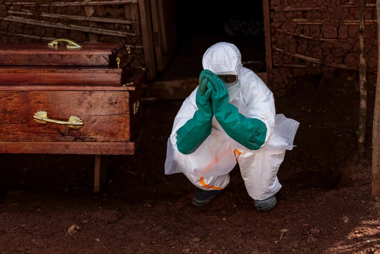 Một nhân viên y tế ngồi bên cạnh quan tài của một nạn nhân nghi mắc Ebola bên ngoài một ngôi nhà ở Mongbwalu, Democratic Republic of the Congo, hôm Chủ nhật, 24/5. Đợt bùng phát Ebola đang lan rộng nhanh chóng tại Cộng hòa Dân chủ Congo chỉ mới thu hút sự chú ý của thế giới hơn một tuần qua, nhưng hiện đã trở thành đợt bùng phát lớn thứ ba từng được ghi nhận. Theo World Health Organization (WHO), đợt dịch tập trung chủ yếu ở miền đông quốc gia châu Phi này đã khiến ít nhất 238 người tử vong và hơn 1.000 ca nghi nhiễm tính đến nay. Dịch bệnh do chủng Bundibugyo – một biến thể hiếm gặp của virus Ebola – gây ra, đồng thời đã lan sang nước láng giềng Uganda. Uganda ghi nhận ít nhất 7 ca liên quan đến ổ dịch, trong đó có một trường hợp tử vong. Ebola có thể gây tử vong ở khoảng 25% đến 90% số người mắc bệnh. Các nhà khoa học hiện đang khẩn trương nghiên cứu các loại vaccine và phương pháp điều trị mới nhằm kiểm soát đợt bùng phát này, tuy nhiên giới chức nhấn mạnh rằng hiện vẫn chưa có vaccine hoặc thuốc điều trị nào được phê duyệt đối với chủng virus đang gây dịch. (Nguồn: Getty Images)