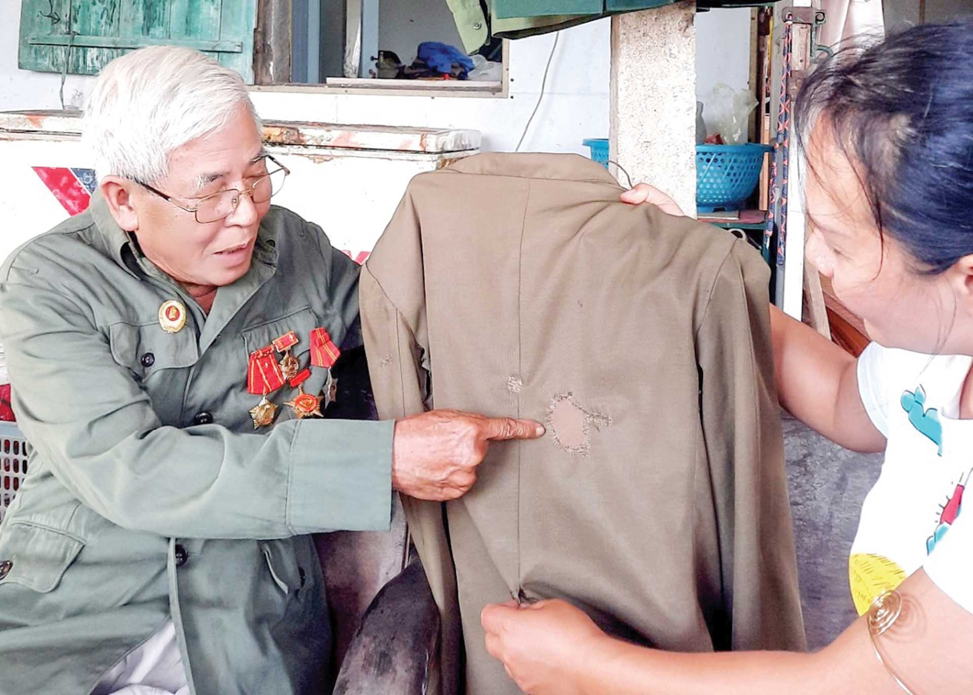 Ông Lê Mai cho xem chiếc áo, cháy do bom napan đã được vợ vá lại mà nay ông vẫn nâng niu như một kỷ niệm một thời chuyến đầu cùng các bạn Lào. (Ảnh: Hạnh Mi)