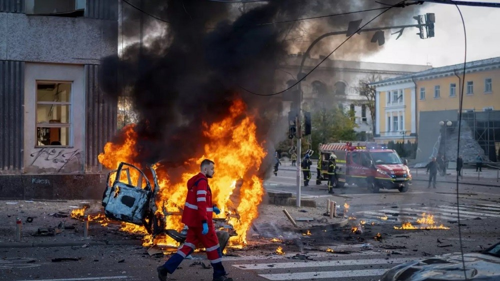 (10.11) Lính cứu hỏa Ukraine đi ngang qua một chiếc xe oto bốc cháy sau đợt tấn công bằng tên lửa của Nga tại Kiev, Ukraine ngày 10/10. (Nguồn: AP)