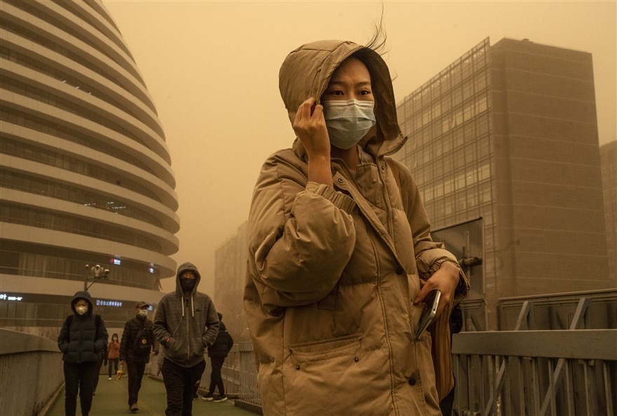 Người dân Bắc Kinh, Trung Quốc đeo khẩu trang và đội mũ chùm kín đầu khi đi ra đường trong trận bão cát, ngày 15/3. Thủ đô của Trung Quốc và một vùng rộng lớn ở phía Bắc đất nước đã bị bao trùm trong trận bão cát tồi tệ nhất một thập kỷ qua, buộc hàng tră