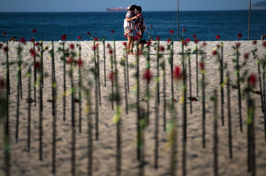 Hai người ôm nhau bên những bông hoa hồng do tổ chức phi chính phủ Rio de Paz đặt trên bãi biển Copacabana, Rio de Janeiro, để tưởng nhớ nửa triệu người đã qua đời vì Covid-19 tại Brazil, ngày 20/6. (Nguồn: Getty)
