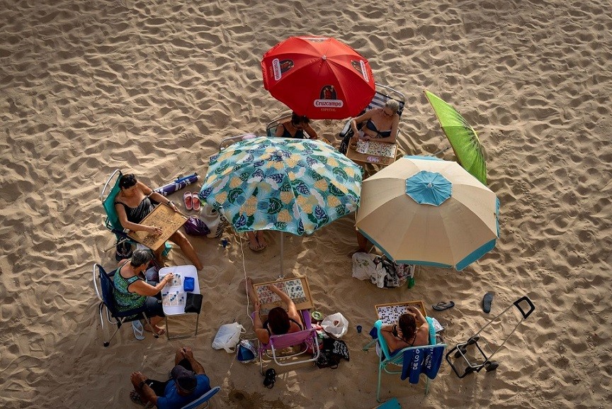 Nhóm phụ nữ chơi bài khi ngồi dưới những chiếc ô trên bãi biển ở Cadiz, Tây Ban Nha, ngày 13/6. Các nước ở châu Âu đang trải qua những ngày ghi nhận nhiệt độ cao nhất trong năm. (Nguồn: AP)